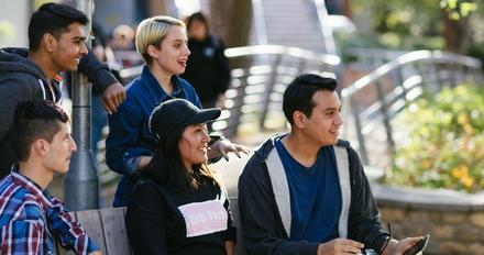 group of five students sitting together on leafy campus