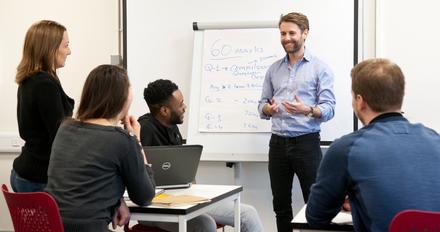 Man standing against a white board talking to students