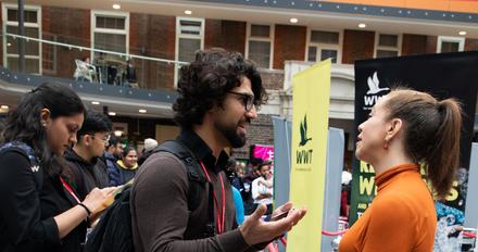 A young man talks to a young woman at an event in a building