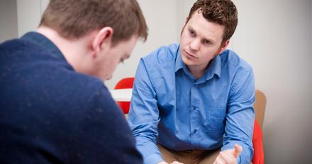A person sitting on a couch talking to a therapist. They are engaged in a conversation about mental health and social work.