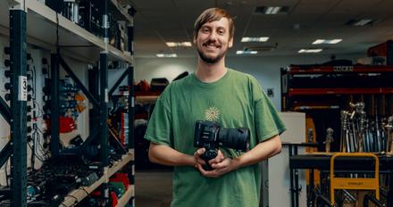 A smiling film student in a room of technical equipment