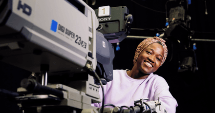 Female student with headscarf stands behind the  camera in the middlesex university tv studio