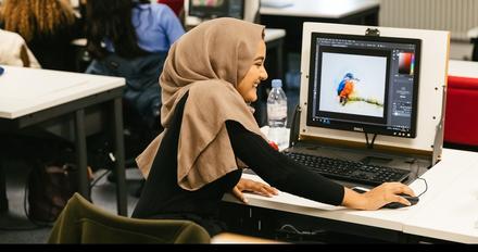 A woman wearing a hijab is focused on her computer screen as she works diligently.