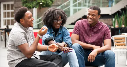 3 students sitting on a courtyard engaged in conversation