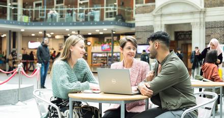Staff sitting in the Quad building looking at a laptop and talking