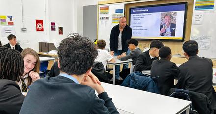 Male school pupils in a classroom watching an adult male standing up at a whiteboard