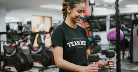 A gym goer smiling with a dumbell in their hand, in the Fitness Pod.