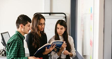 three students study book in front of white board