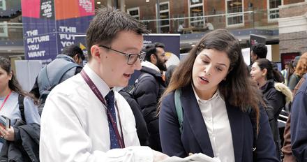 two smartly dressed people having conversation, looking at clipboard