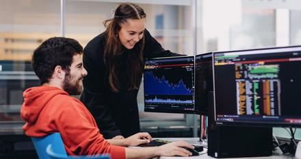 A female and male student, both smiling, while studying at our Financial Markets lab