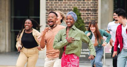 Diverse group of students running together outdoors on campus, smiling and laughing during a university open day activity