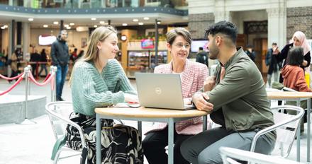 Professor and students sitting at table with a laptop.