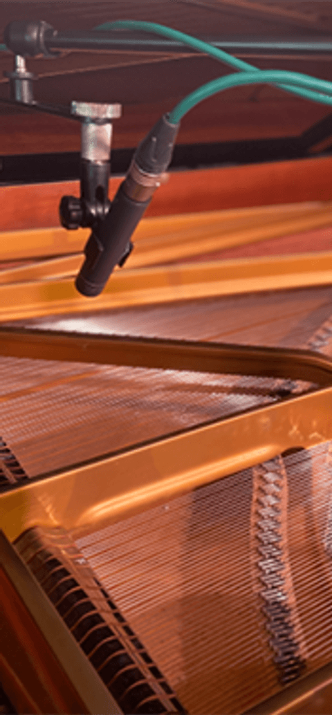 Close-up of microphones recording inside an open grand piano, capturing strings and hammers for a BA (Hons) Music for Film and Games course.