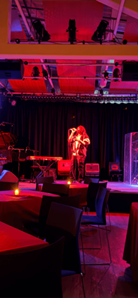 Live band performing on stage in a moody, red-lit music venue with candlelit tables in the foreground