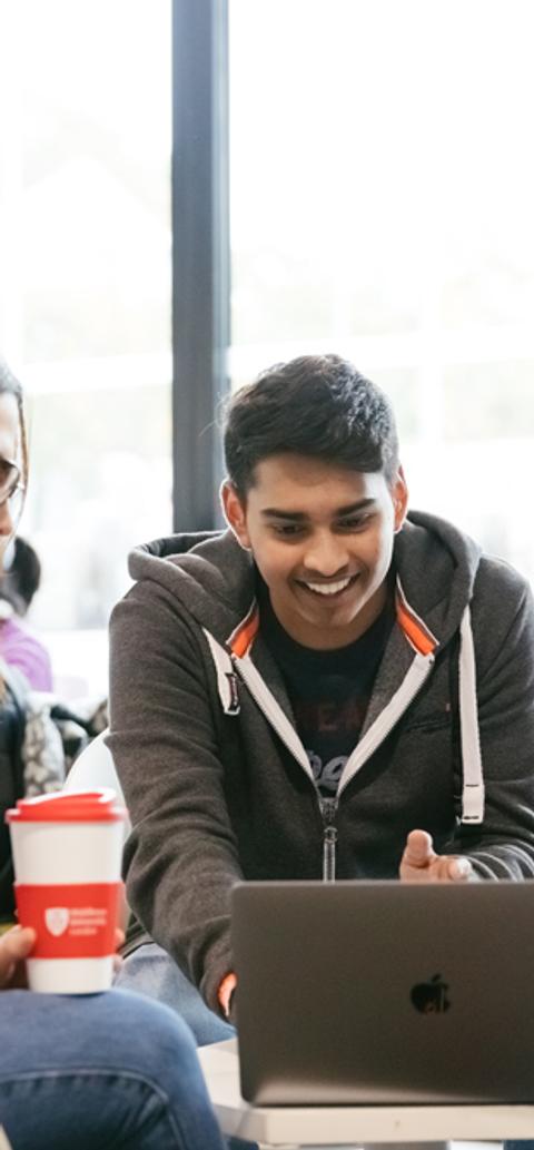 A group of three students gathered round a laptop in a cafe area