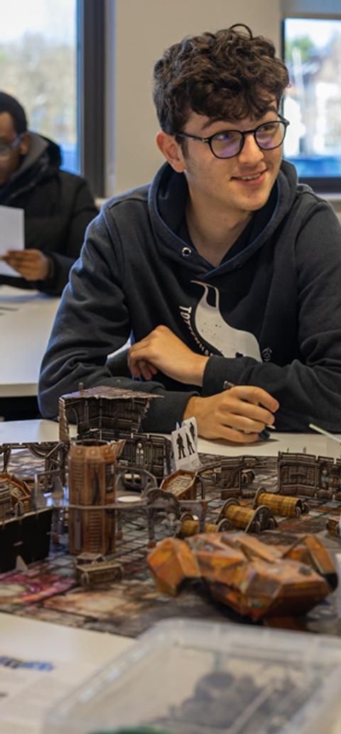 A group of male students sat around games pieces on a table