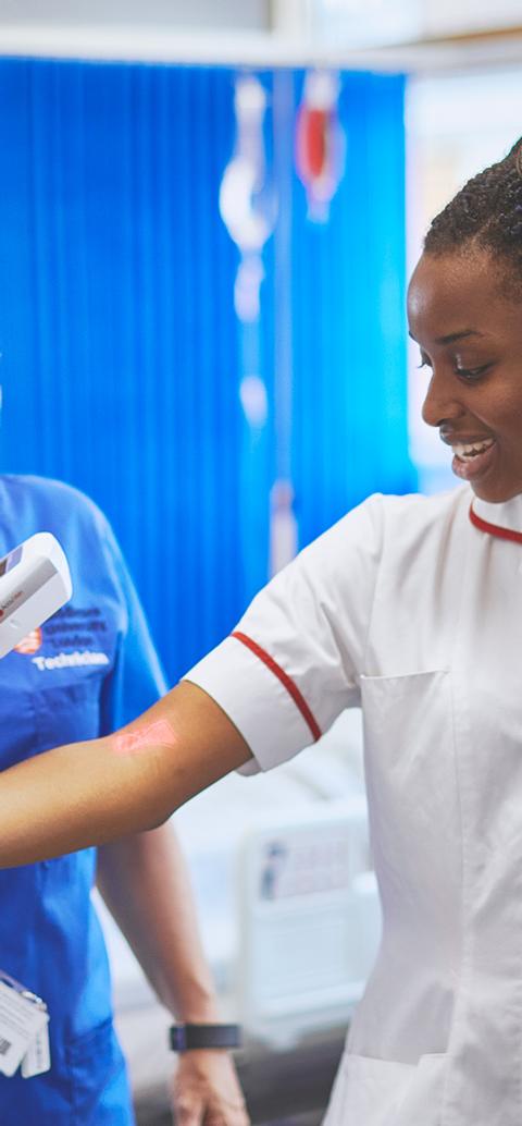 Student nurse practising clinical assessment with a tutor in a simulated hospital ward using a handheld medical device