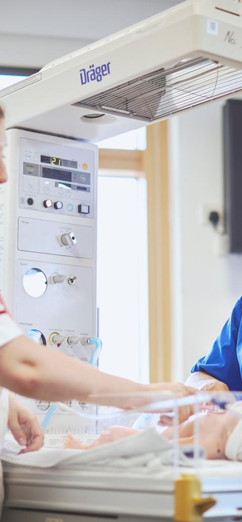 A student nurse and instructor provide care to an infant mannequin during a paediatric nursing simulation.