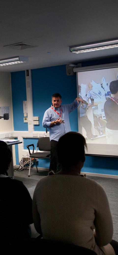 A lecturer leads a workshop on mental health practice, presenting a clinical scenario to students in a classroom setting