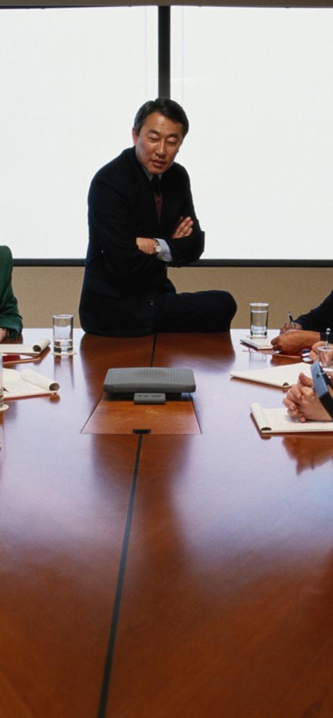 Professionals participate in a meeting around a conference table during a leadership discussion.