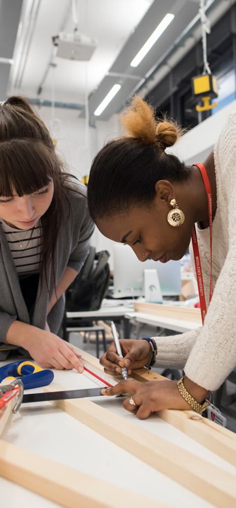Students measure and mark wooden materials during an interior design workshop.