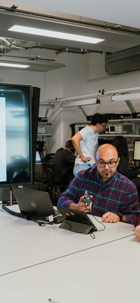 Product design students collaborate with a lecturer on an electronics prototype in a university workshop.