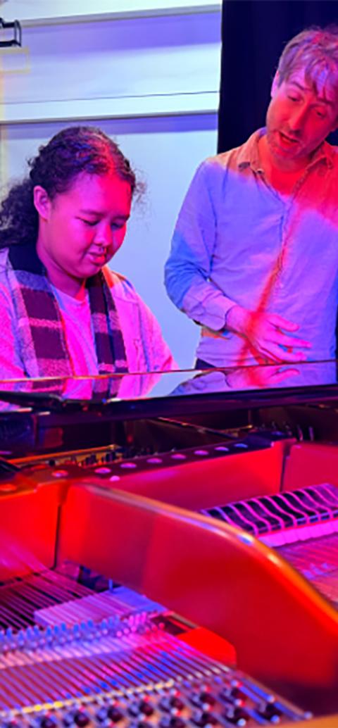 Student at piano with teacher watching on.