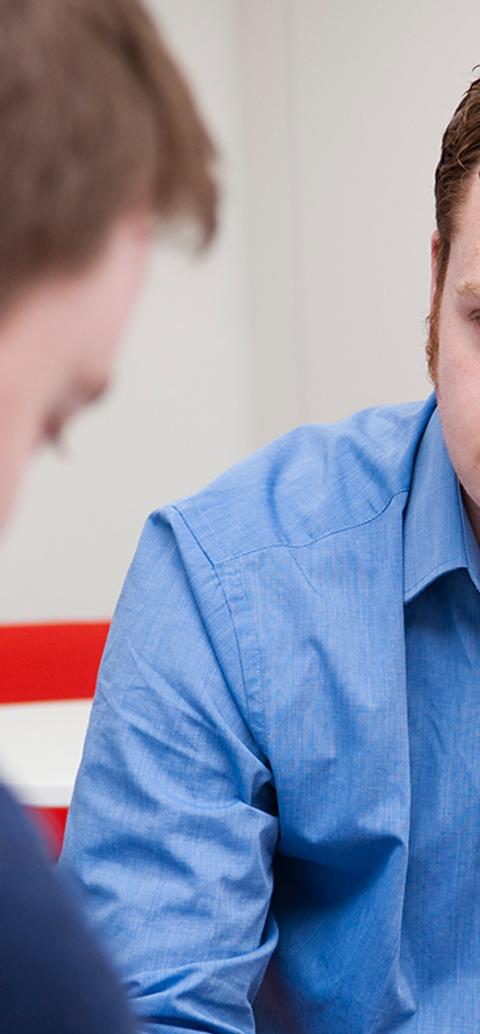 student sat in blue shirt sat down facing another man