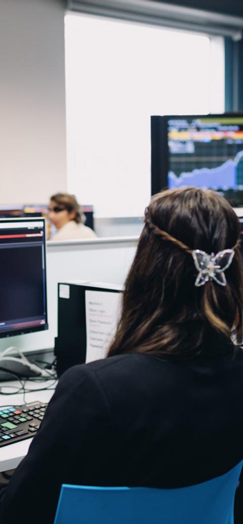 Two young people looking at financial forecasts on computer monitors