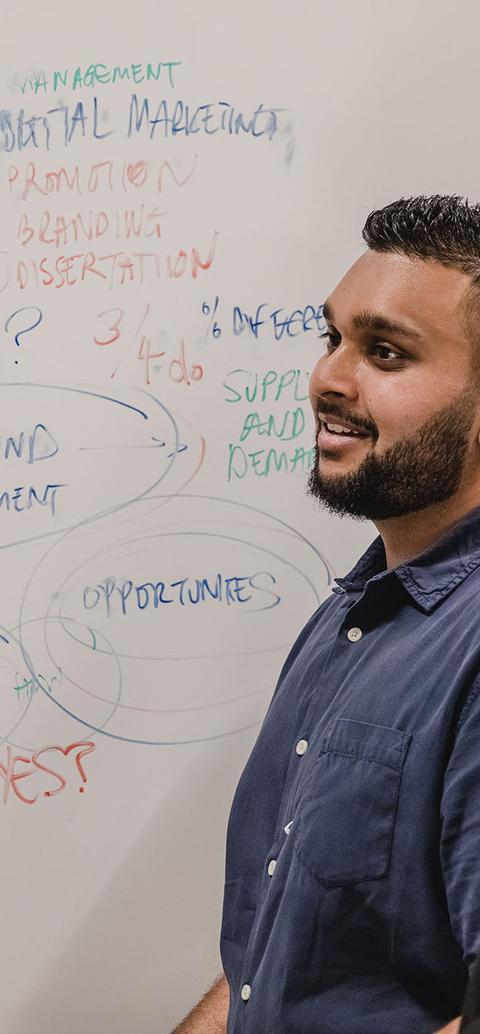 two students stand in front of whiteboard with business plans