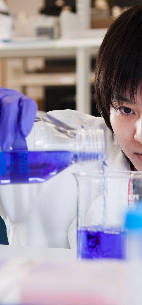 oriental student in a lab mixing chemicals