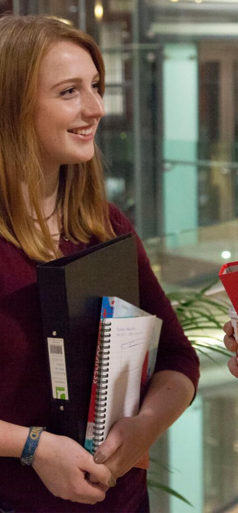 two women holding accounting textbooks have a friendly conversation