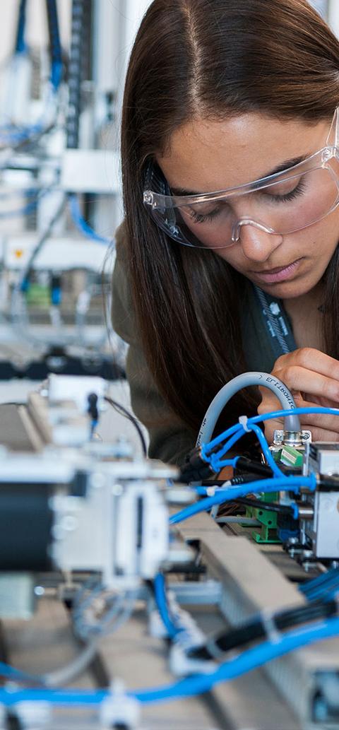 female student wearing googles works on circuitry with small screwdriver