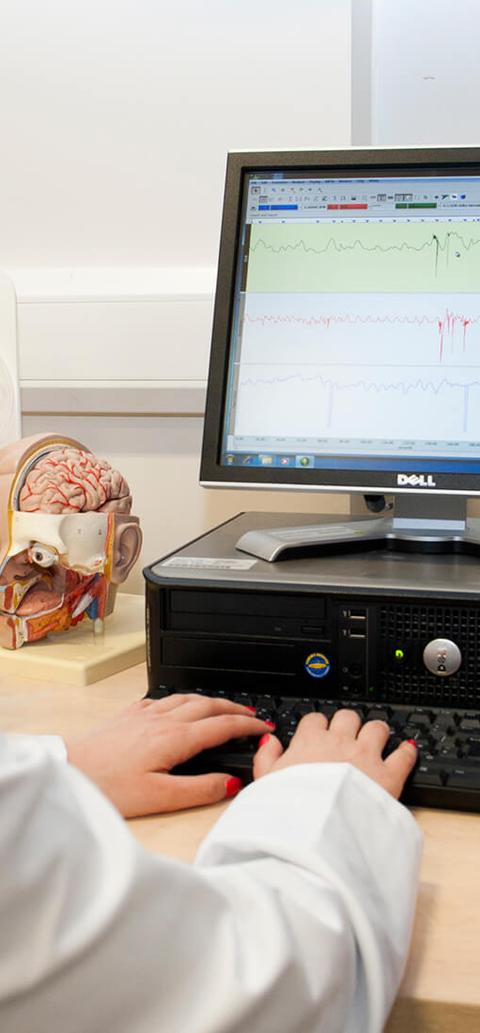 A female student with a blonde bob haircut sitting at a desk, looking at a computer screen with data on it