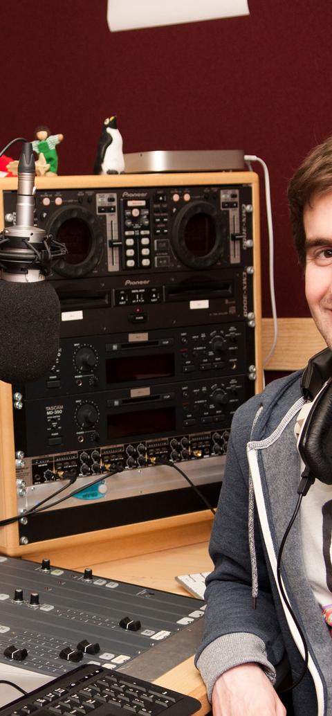 Male student wearing headphones sitting in front of a music mixer device