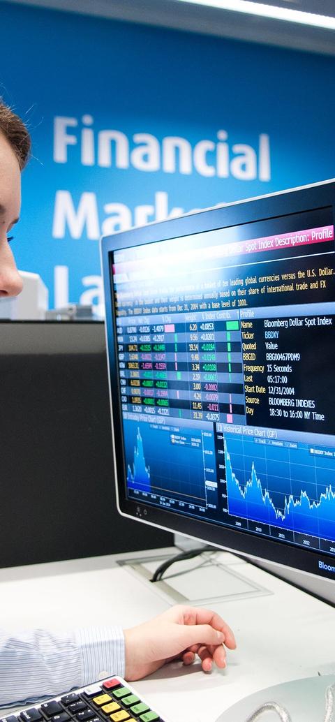 A female student sitting in front of a computer monitor displaying financial data in the Financial Markets Lab