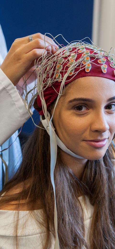 A woman sits with a therapist who is applying electrodes to a cap on her head