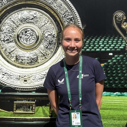 A young wpoman in a dark t shirt stands in front of a large silver dish