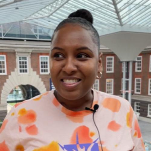 Portrait of Zara Johnson, postgraduate digital marketing student, standing in front of windows and a covered atrium