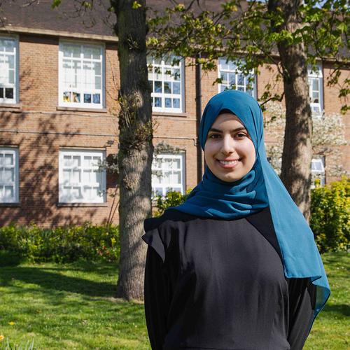 Student Duha posing in front of red bricked building