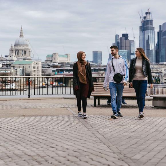 3 middlesex university students walk along the thames with st pauls in the background