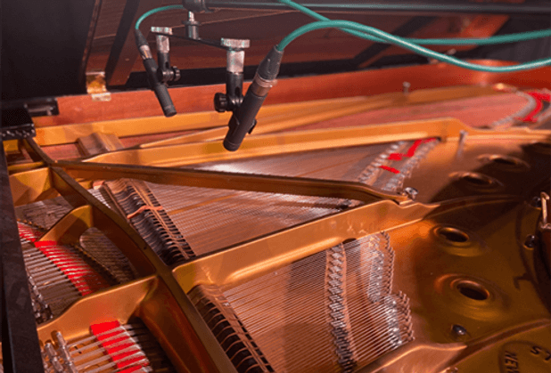 Close-up of microphones recording inside an open grand piano, capturing strings and hammers for a BA (Hons) Music for Film and Games course.