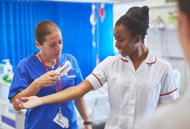 Student nurse practising clinical assessment with a tutor in a simulated hospital ward using a handheld medical device