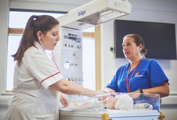 A student nurse and instructor provide care to an infant mannequin during a paediatric nursing simulation.
