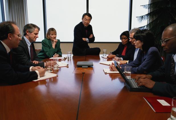 Professionals participate in a meeting around a conference table during a leadership discussion.