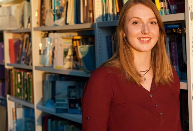 Female student stood in front of library shelf with books behind