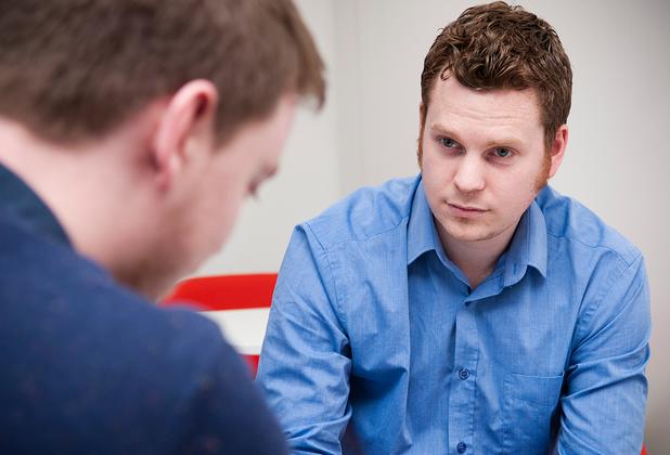 student sat in blue shirt sat down facing another man