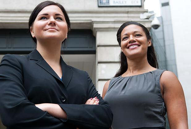 two smiling woman wearing business attire standing outside a building