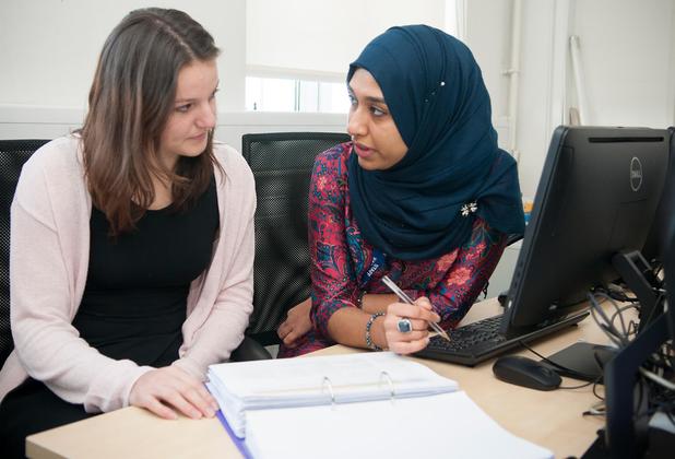 Two female students (one wearing a headscarf) sitting at a desk, talking