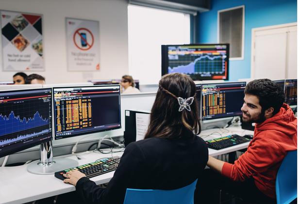 Two young people looking at financial forecasts on computer monitors